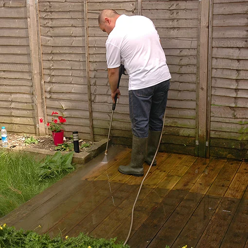 Pressure washing timber decking beside a garden fence